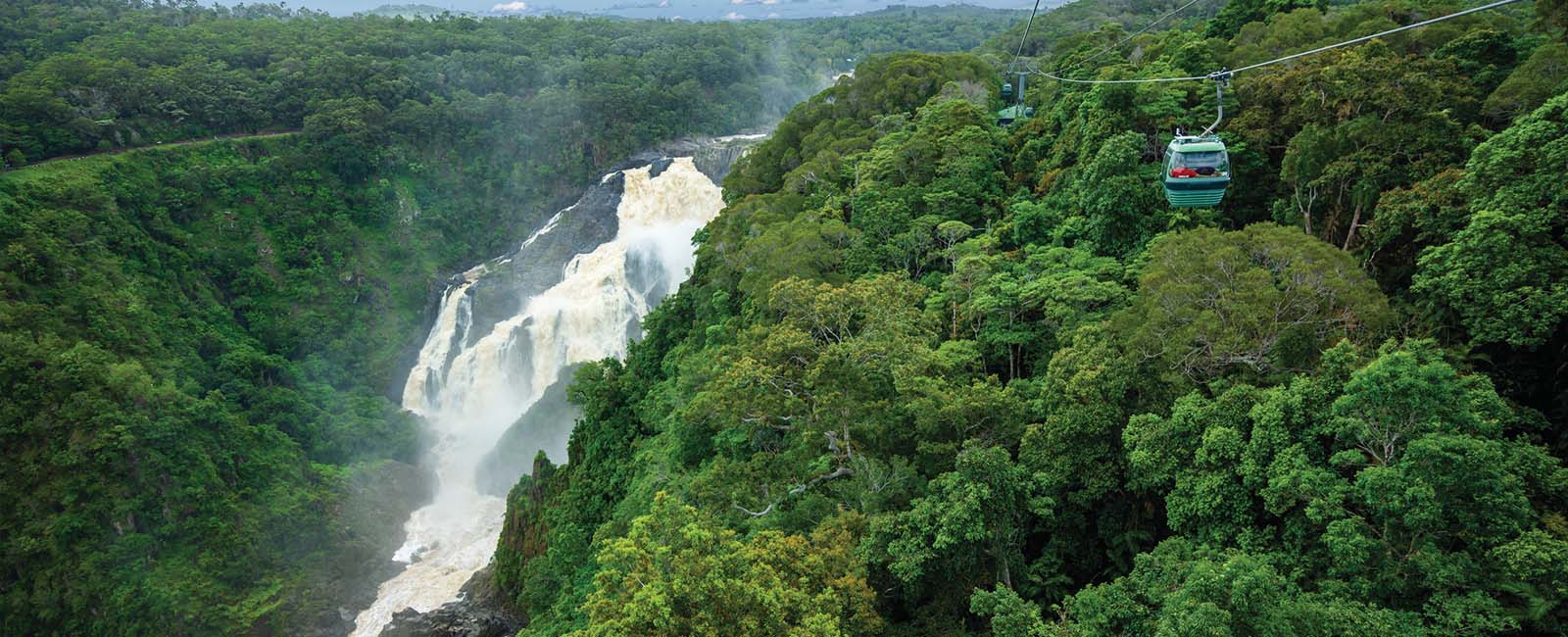 A gushing waterfall in the rainforest with a cable car overhead. 