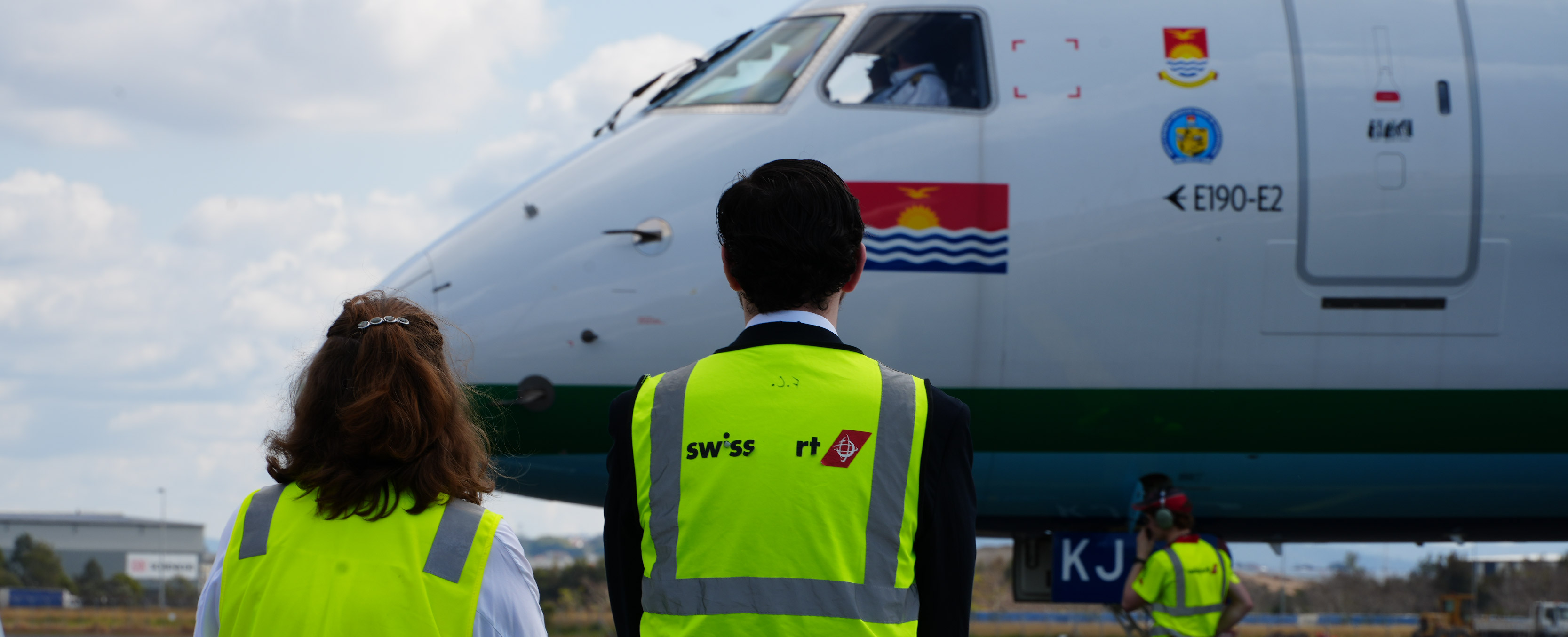 two people in high-vis watch as plane is directed into bay