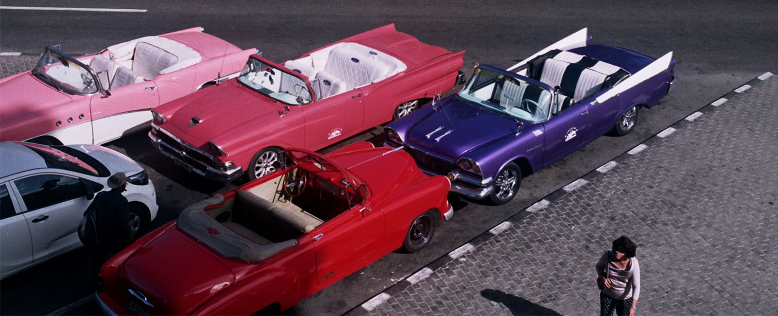 Brightly coloured vintage convertible cars parked on a road