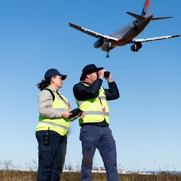 Two airside officers with a Jetstar plane flying overhead Two airside officers with a Jetstar plane flying overhead
